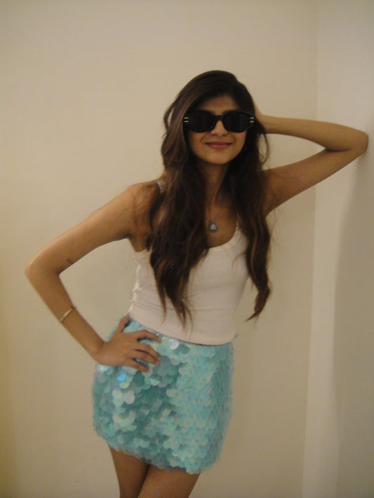 Woman wearing sunglasses and a white top with a blue sequin skirt for ibiza summer 